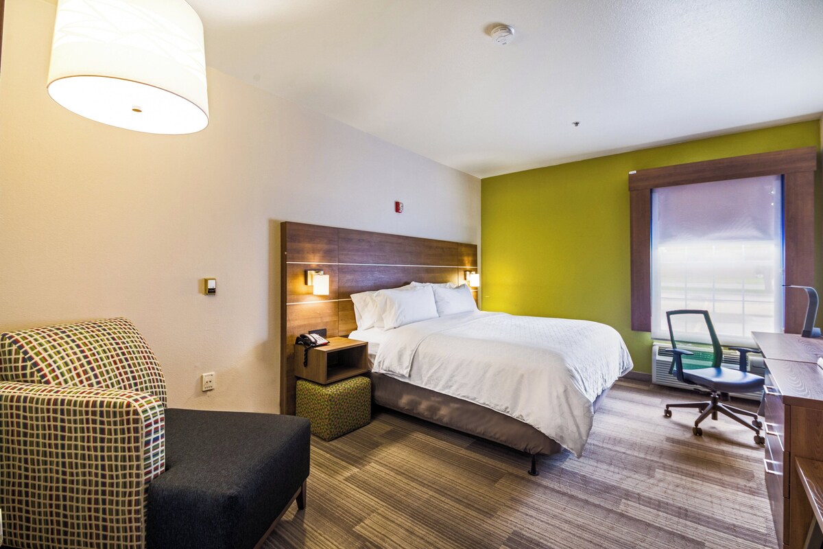 A hotel room with a bed, bedside table, chair, desk, and a window.