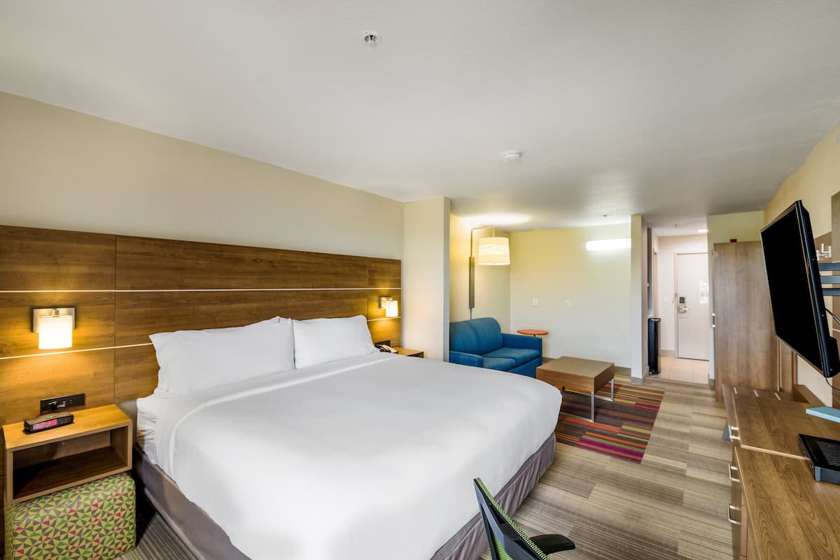 Une chambre d’hôtel avec un grand lit, des tables de chevet, un bureau, une chaise, une télévision et une porte donnant sur une salle de bain.