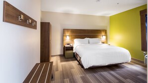 A modern hotel room with a large bed, wooden headboard, bedside lamps, a nightstand, and a wall-mounted light fixture. - Holiday Inn Express Hotel & Suites Columbus by IHG (Columbus)