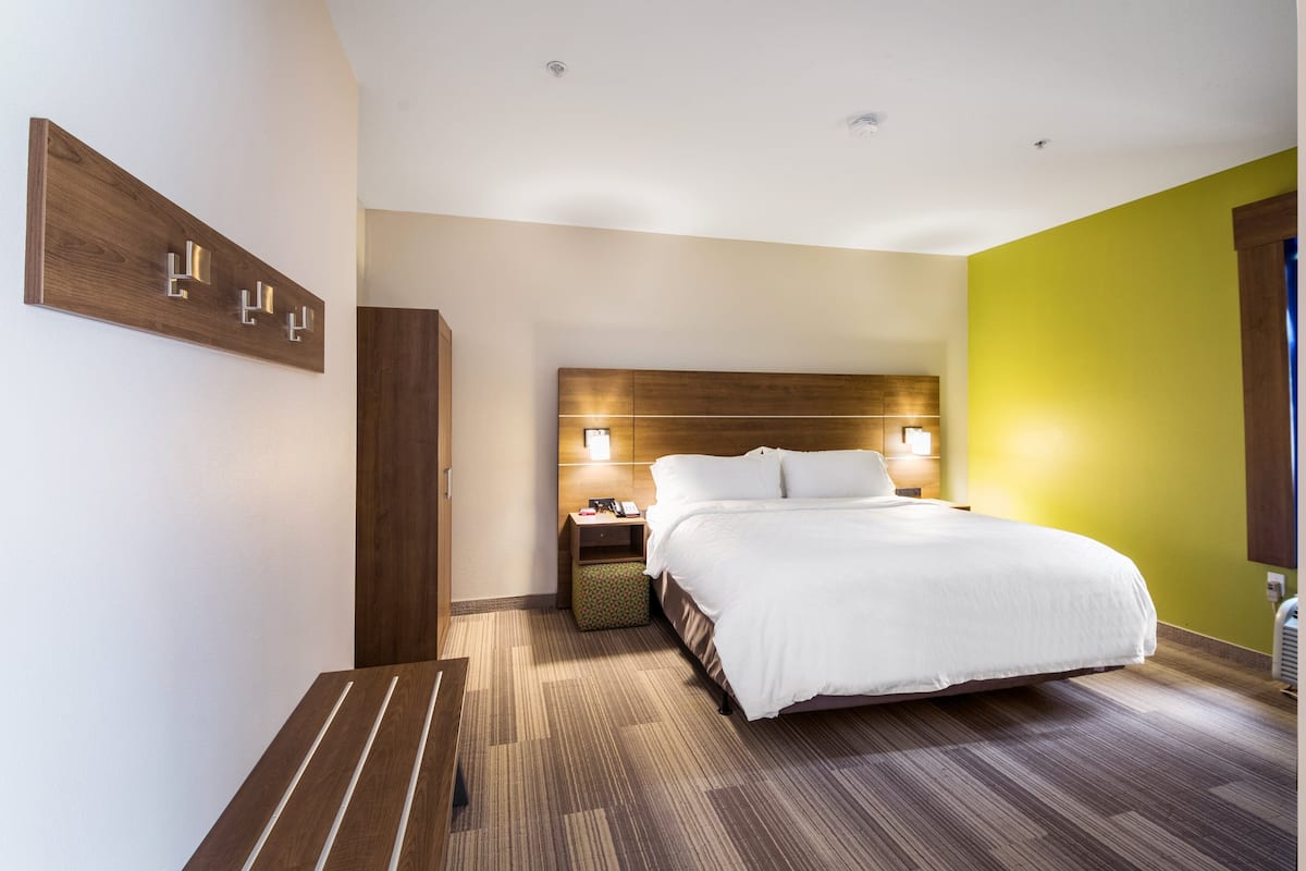 Une chambre d’hôtel moderne avec un grand lit, une tête de lit en bois, des lampes de chevet, une table de chevet et un luminaire fixé au mur.
