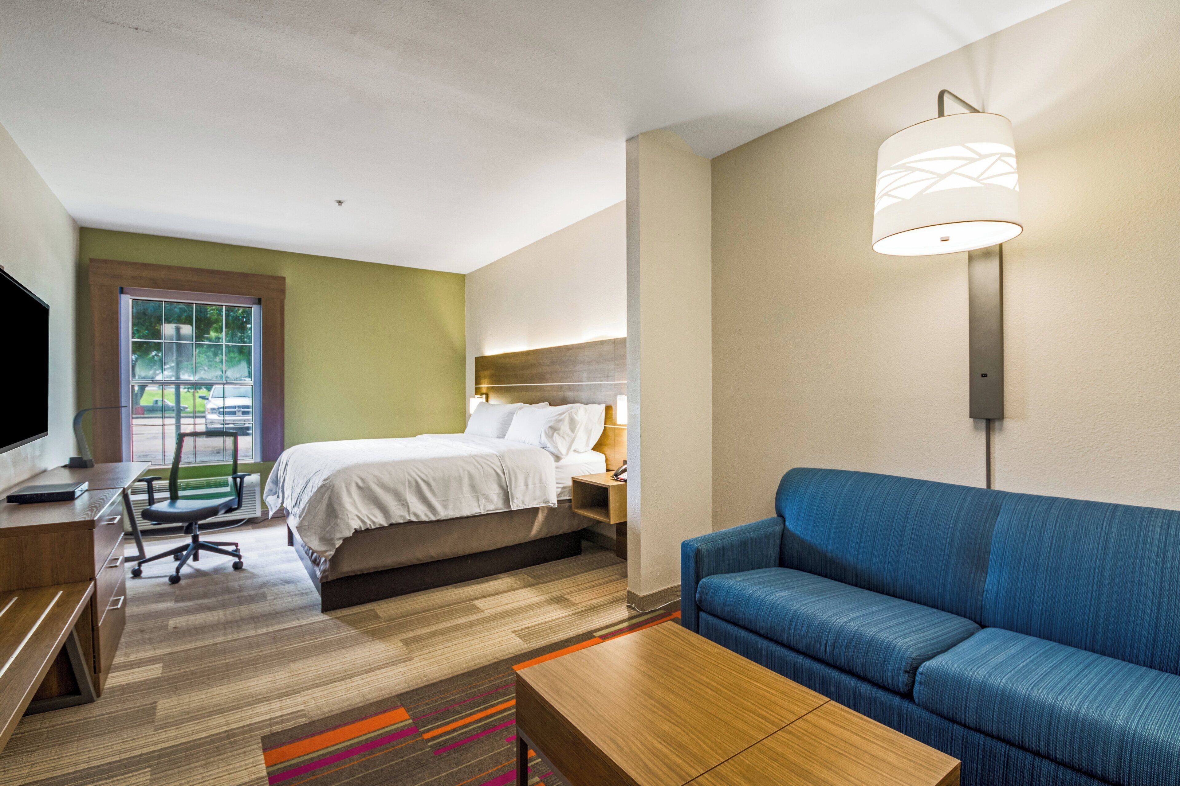 Una habitación de hotel con cama, escritorio, silla, sofá y televisor.