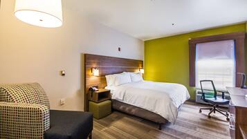 A hotel room with a bed, a desk, a chair, a nightstand, and a lamp.