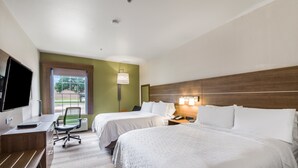 A hotel room with two beds, a desk, a chair, a TV, and a window with a view of trees. - Holiday Inn Express Hotel & Suites Columbus by IHG (Columbus)