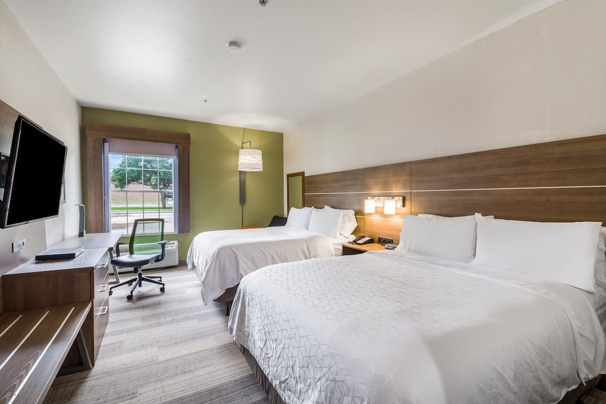 Une chambre d’hôtel avec deux lits, un bureau, une chaise, une télévision et une fenêtre donnant sur des arbres.