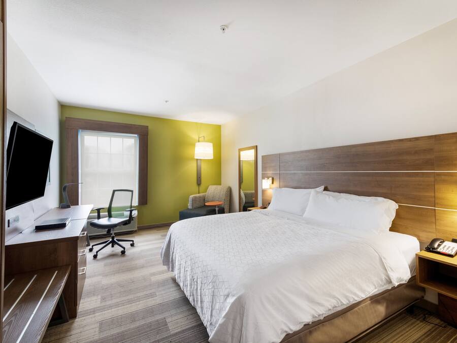 A hotel room with a bed, desk, chair, and a TV.