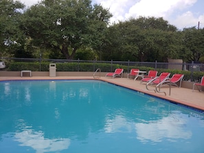 A swimming pool with a tiled edge, surrounded by a low fence and red lounge chairs.