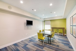 A conference room with a table and chairs, a flat-screen TV mounted on the wall, and a window with blinds. - Holiday Inn Express Hotel & Suites Columbus by IHG (Columbus)