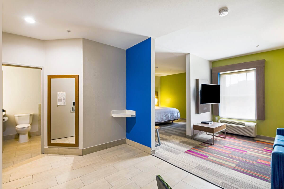 Una camera d'albergo moderna con un letto, una televisione, un tavolino e un tappeto colorato.