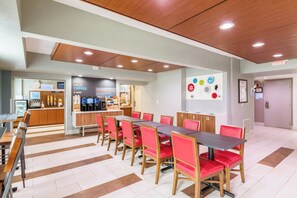 Una cafetería moderna con una mesa larga y sillas rojas, una estación de café y una pared decorada con elementos circulares.