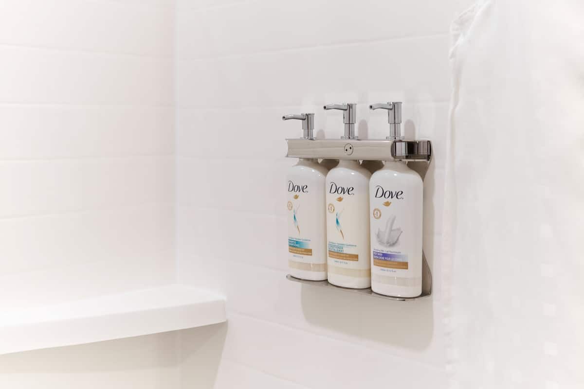 A bathroom with three Dove lotion dispensers mounted on a white tiled wall.