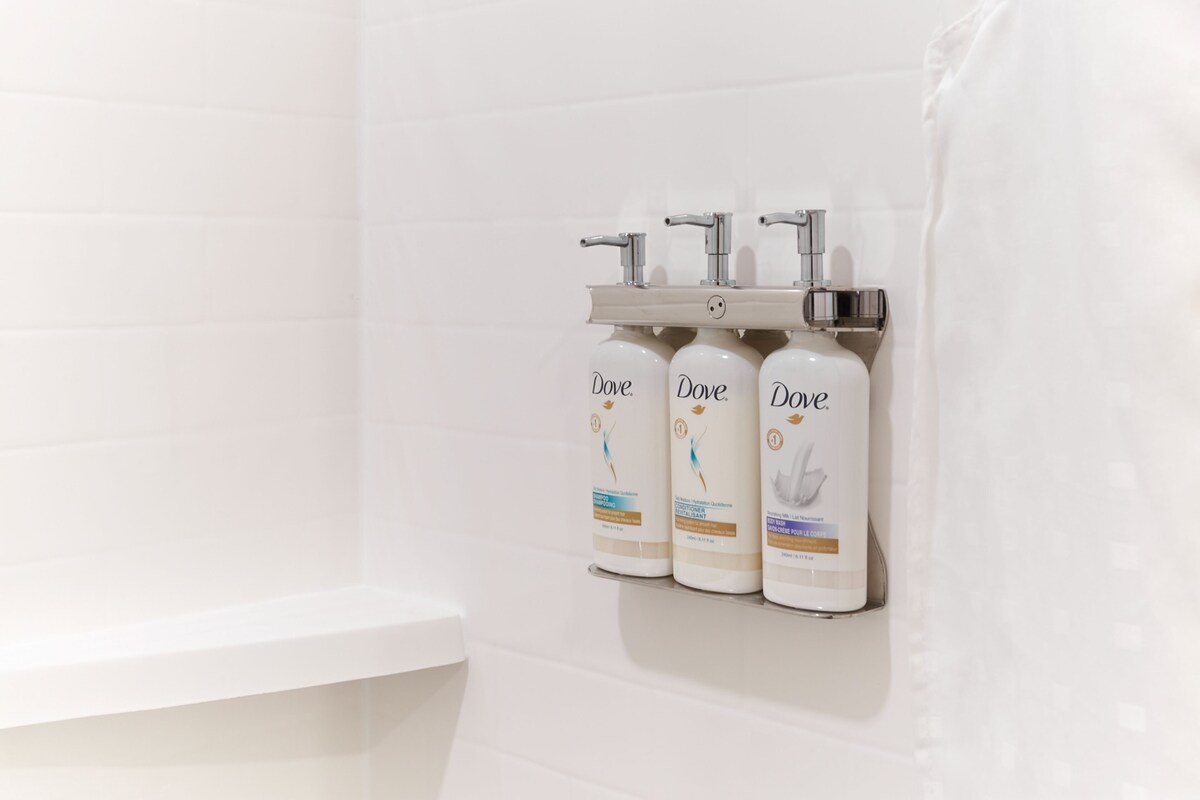 A bathroom with three Dove lotion dispensers mounted on a white tiled wall.