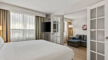 A hotel room with a large bed, a television, a sofa, and a door leading to another room.