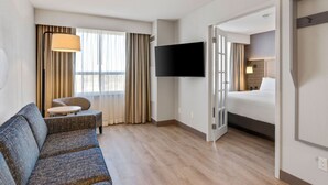 A hotel room with a sofa, a TV mounted on the wall, a bed, and a window with curtains. - Holiday Inn Hotel & Suites Ottawa Kanata by IHG (Ottawa)