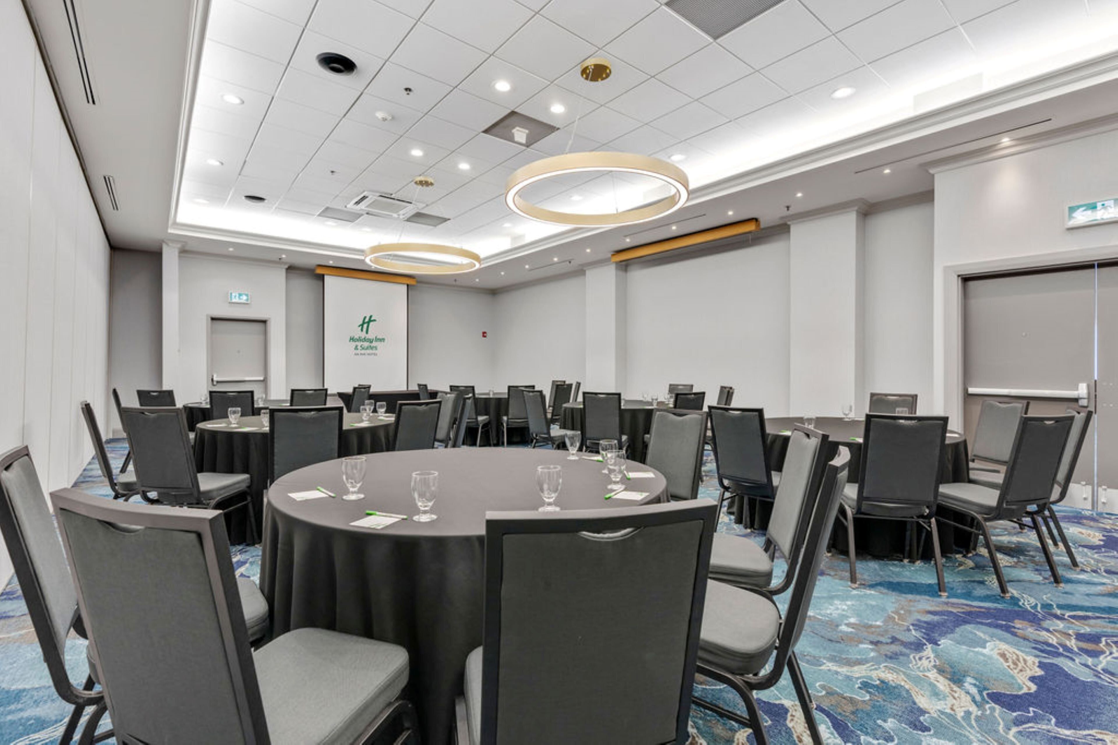 Un salón de conferencias con mesas redondas, sillas y piso cubierto de moqueta azul.