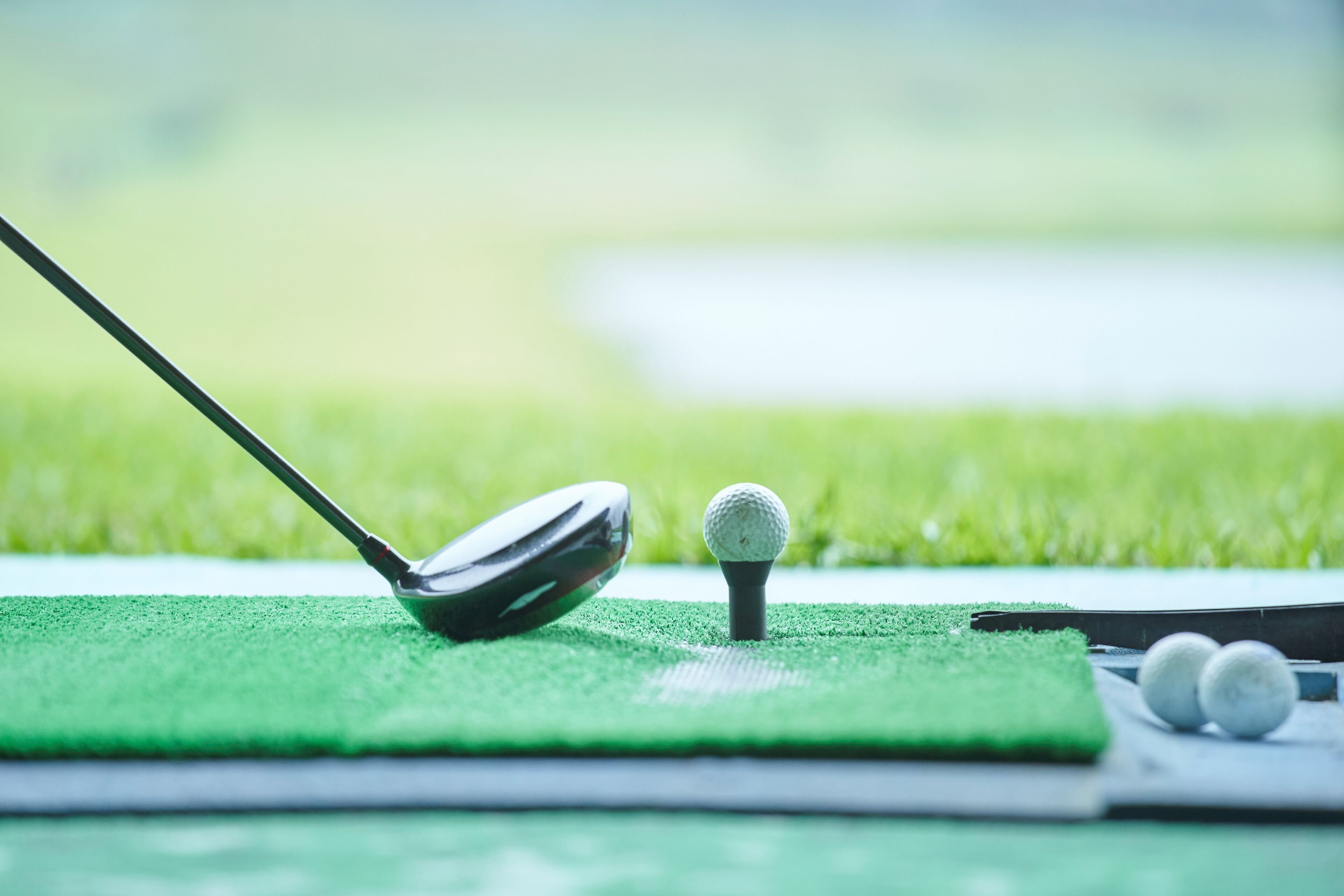 Un palo de golf sobre un tapete verde, con una pelota de golf y dos pelotas de golf adicionales al fondo.