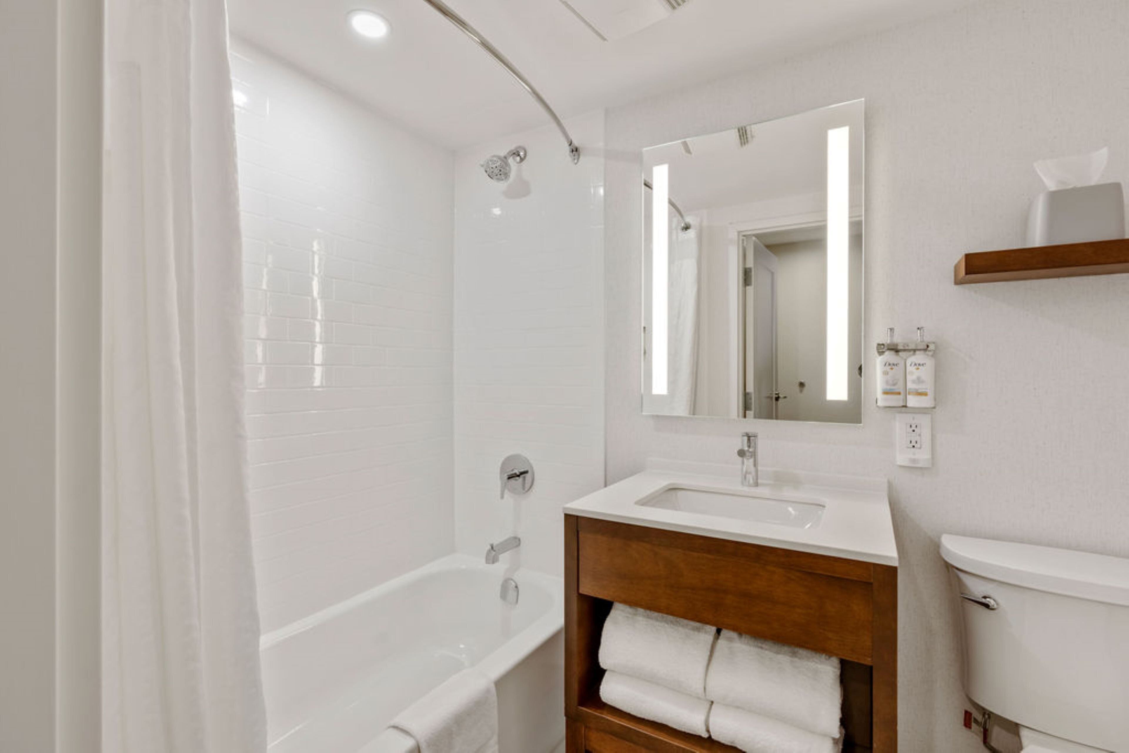 Un baño moderno con una bañera blanca, un tocador de madera, un espejo y un inodoro.