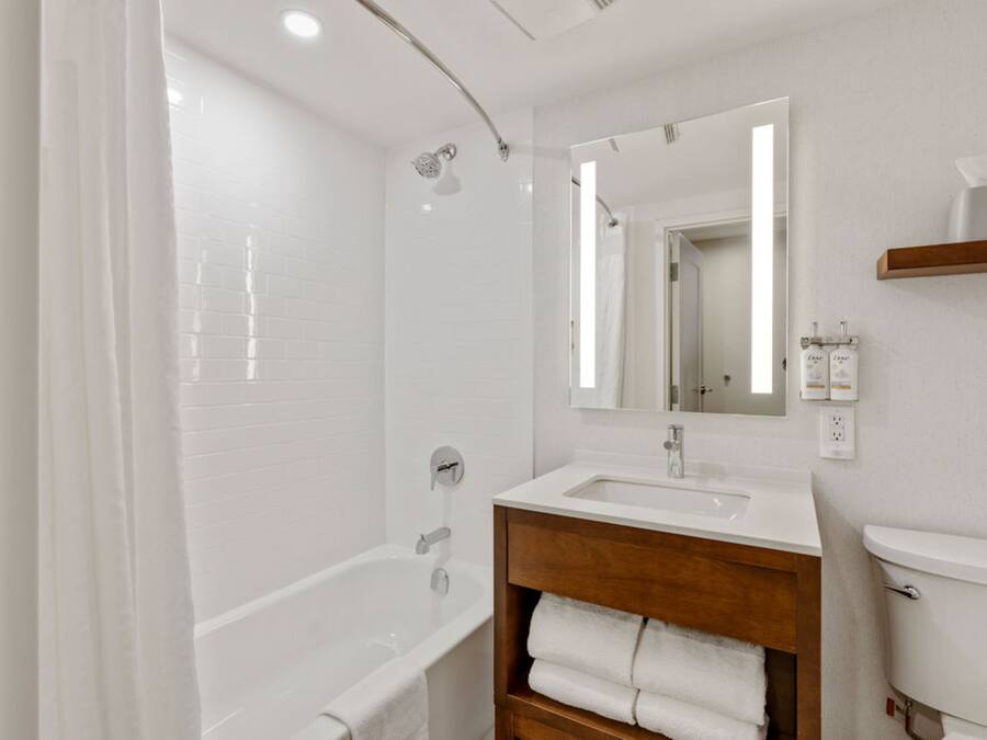 Un baño moderno con una bañera blanca, un tocador de madera, un espejo y un inodoro.