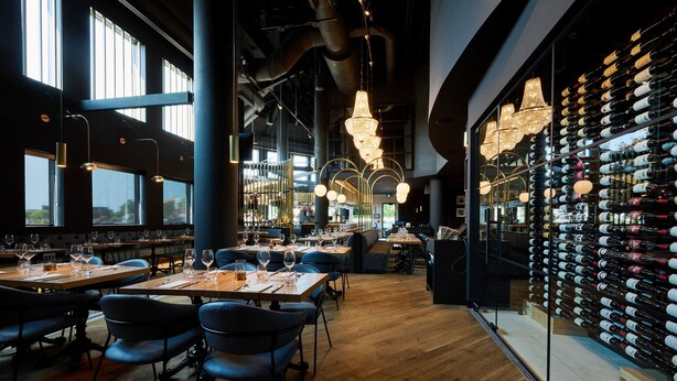 A restaurant with wooden tables and chairs, hanging lights, and a wine rack with bottles. - Holiday Inn Hotel & Suites Ottawa Kanata by IHG (Ottawa)