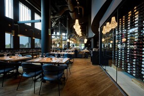 A restaurant with wooden tables and chairs, hanging lights, and a wine rack with bottles. - Holiday Inn Hotel & Suites Ottawa Kanata by IHG (Ottawa)