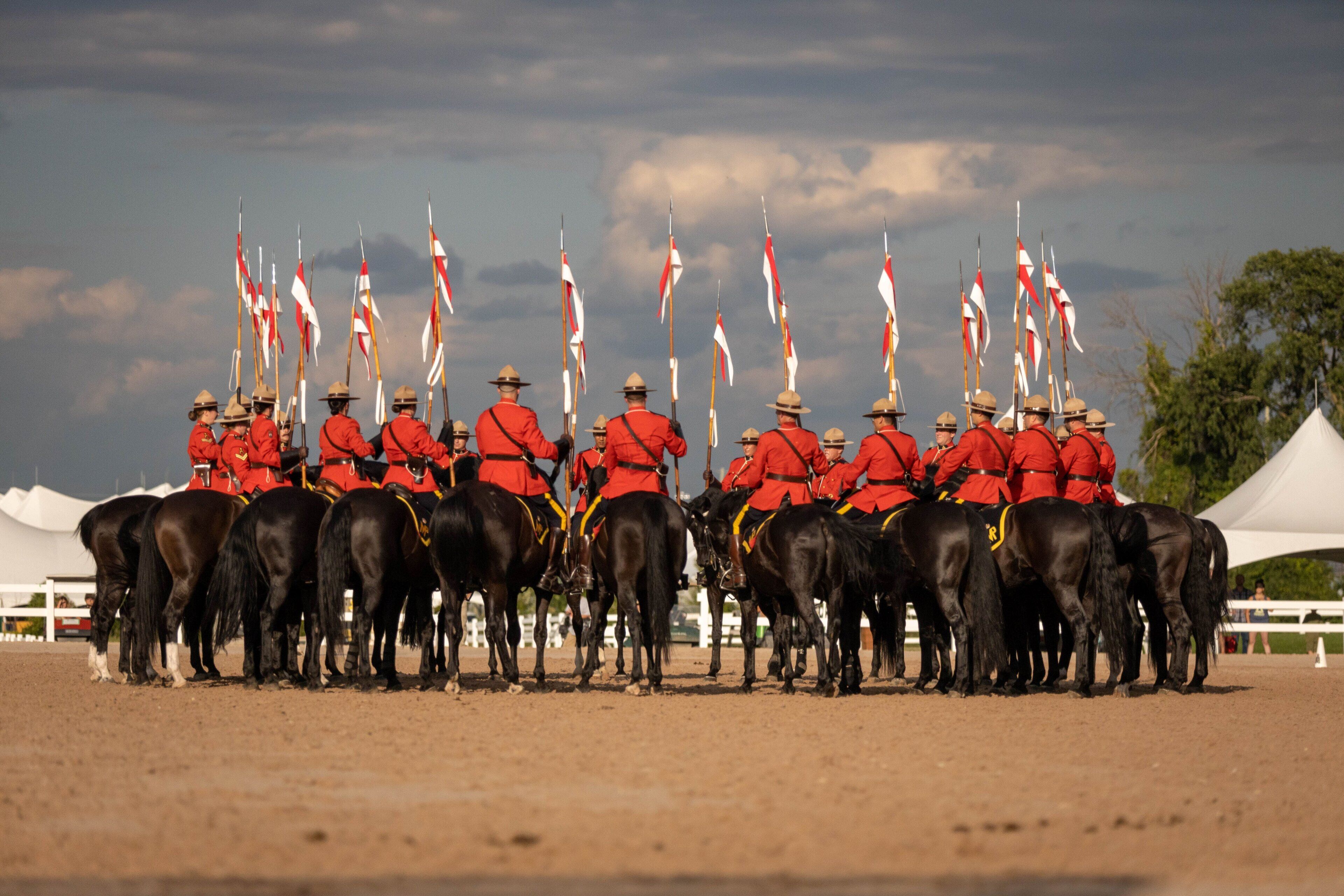 A group of people in red uniforms on horses, standing in formation with flags.