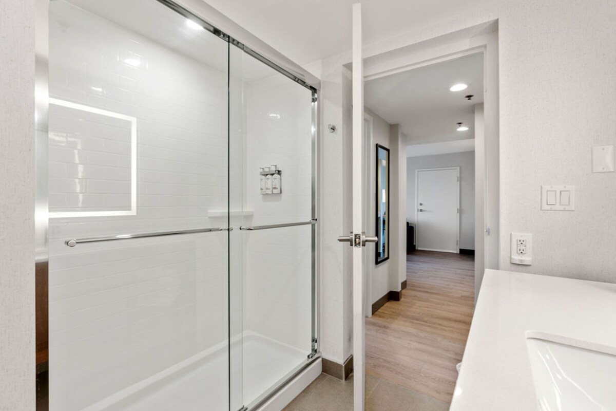 A modern bathroom with a glass shower enclosure, a white sink, and a wooden floor.