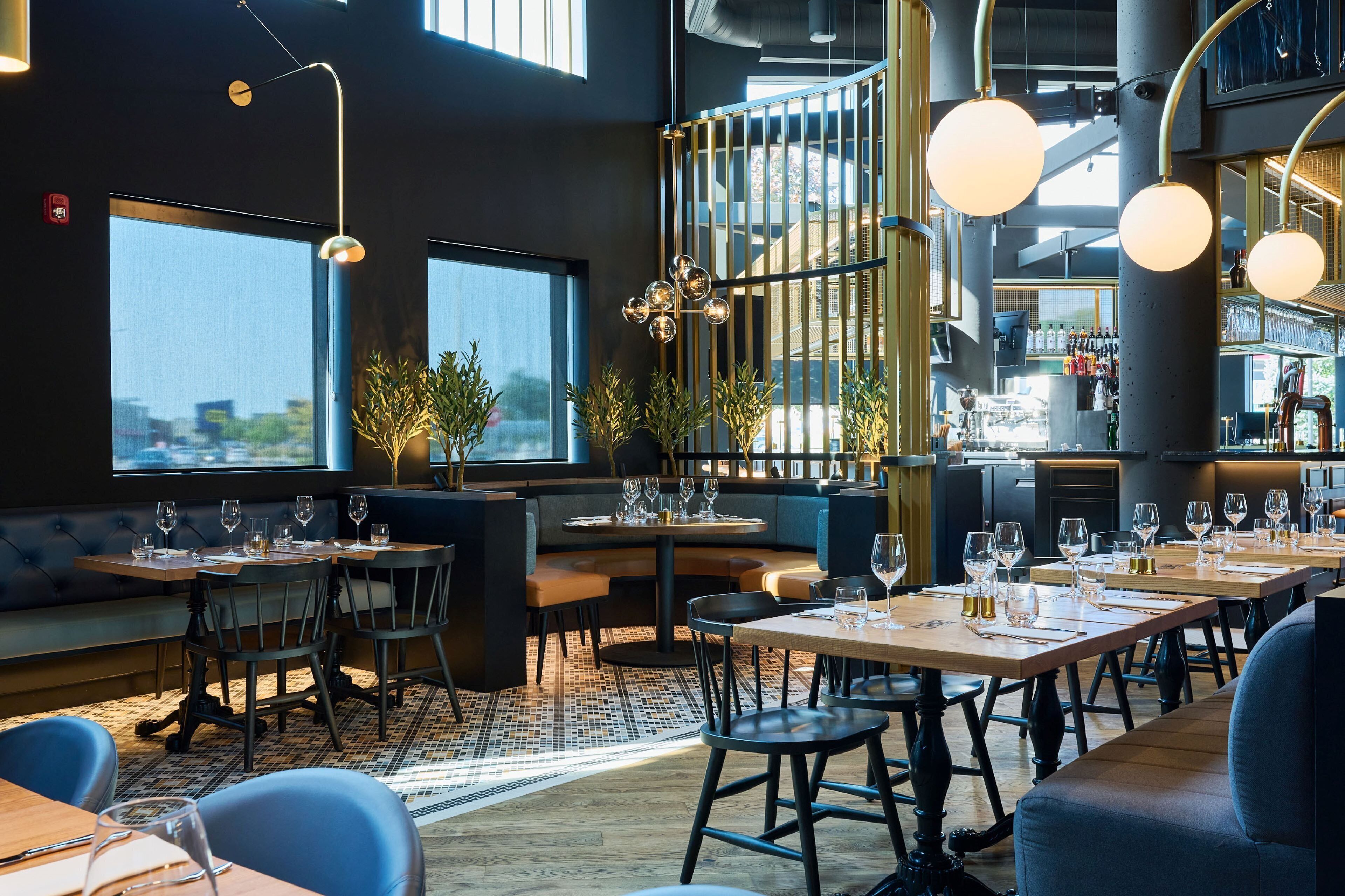 A modern restaurant with high tables and booths, large windows, and a bar area.