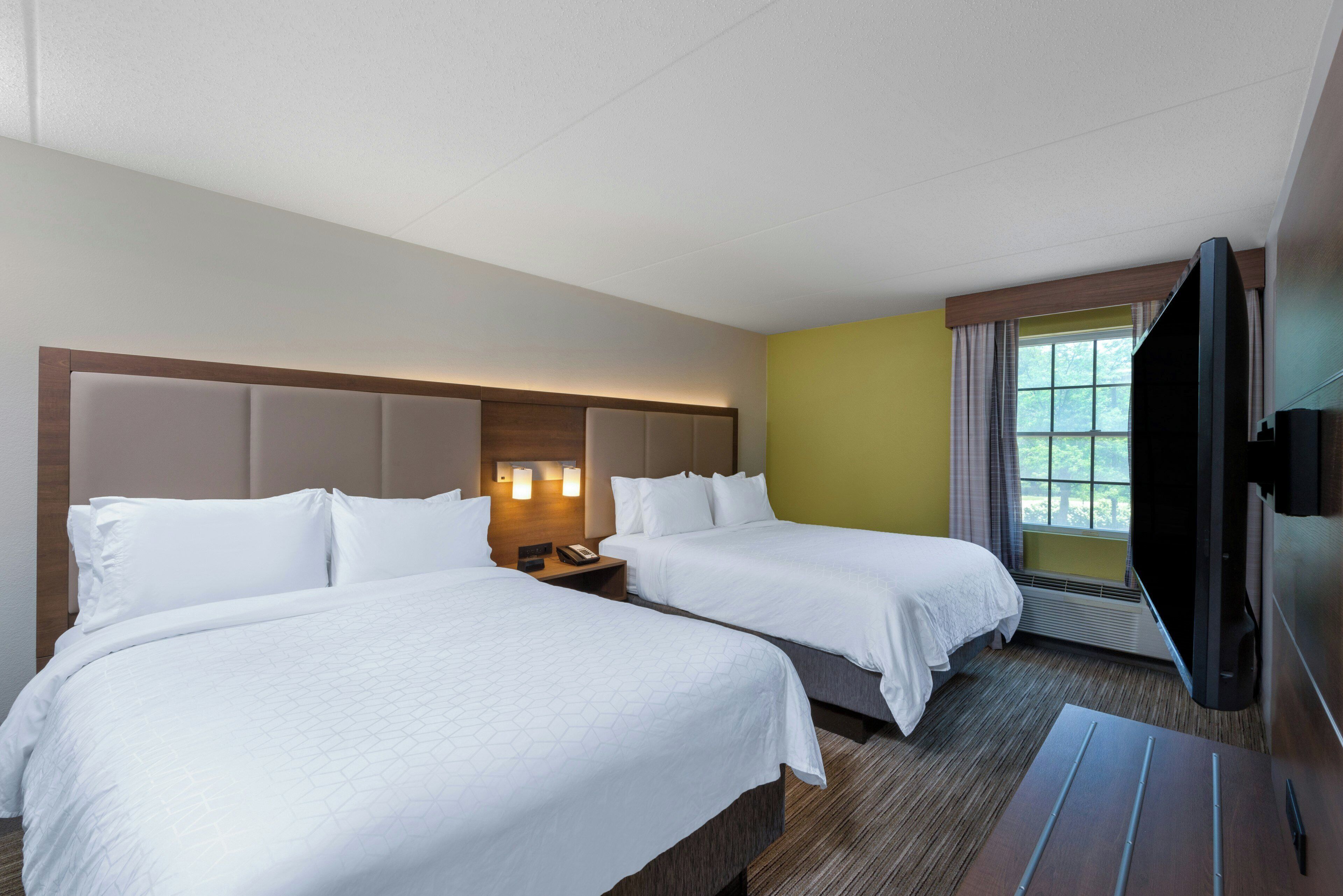 A hotel room with two beds, a flat-screen TV, and a window with curtains.