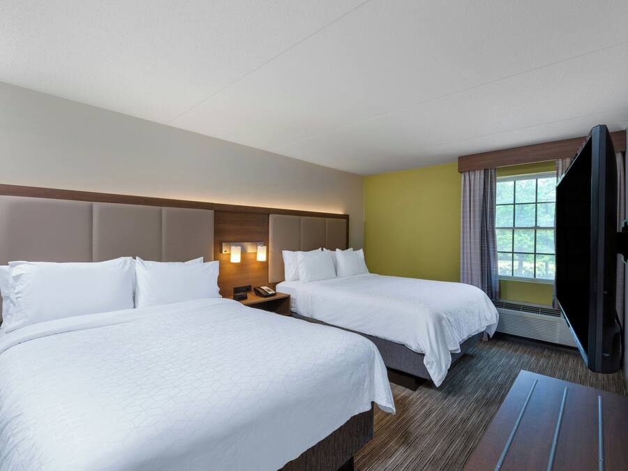 Ein Hotelzimmer mit zwei Betten, einem Flachbildfernseher und einem Vorhangfenster.