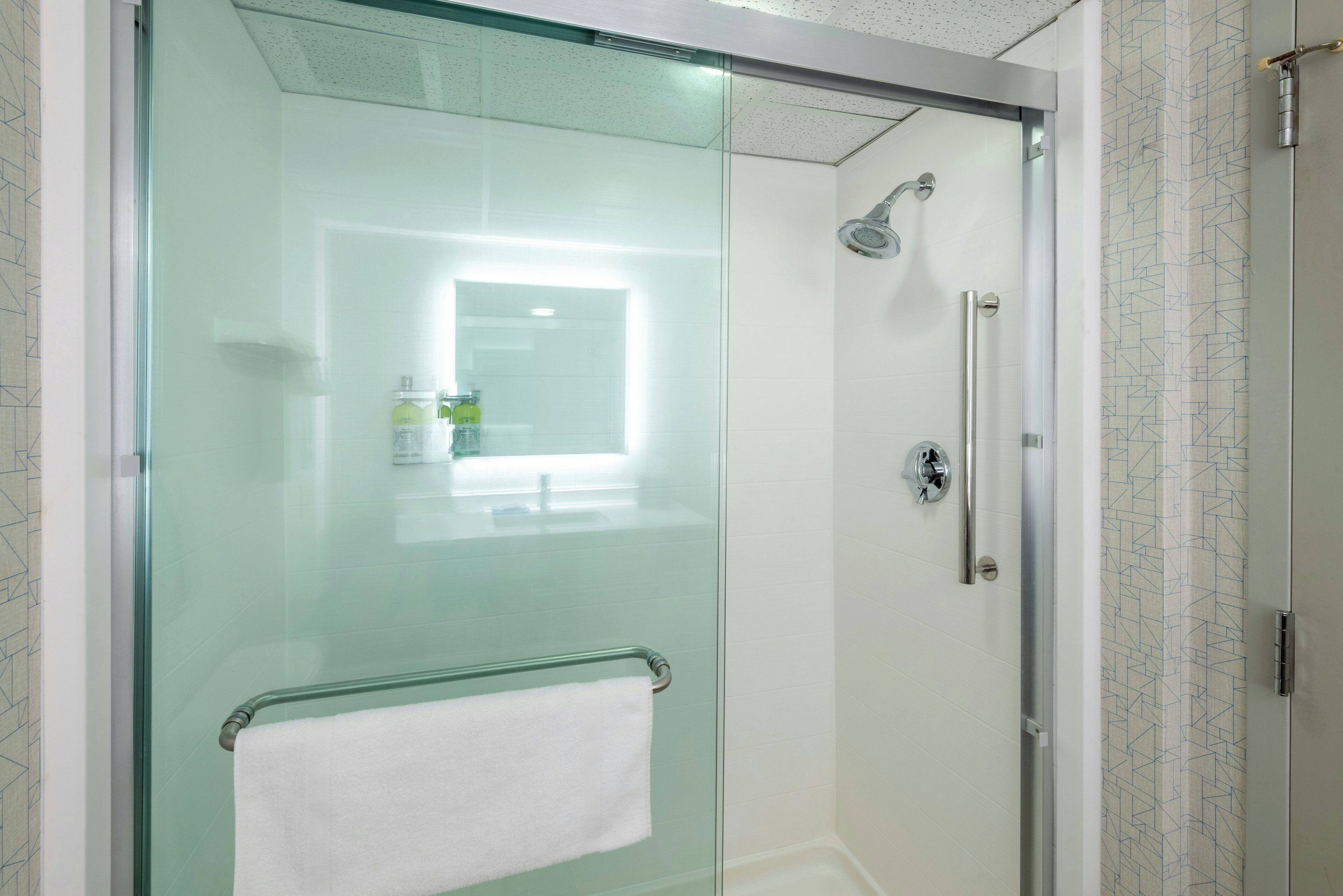 A modern bathroom with a glass shower enclosure, a white towel hanging on a metal rack, and a mirror above the sink.