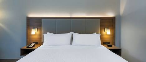 A hotel room with a large bed, two bedside tables, and wall-mounted lamps.
