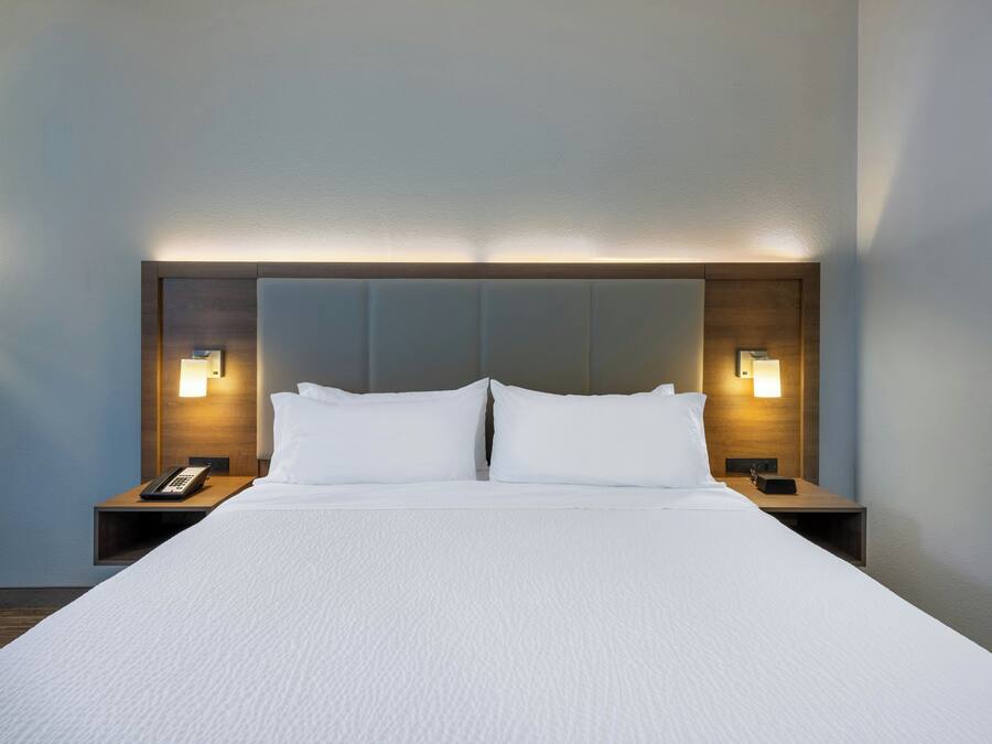 A hotel room with a large bed, two bedside tables, and wall-mounted lamps.