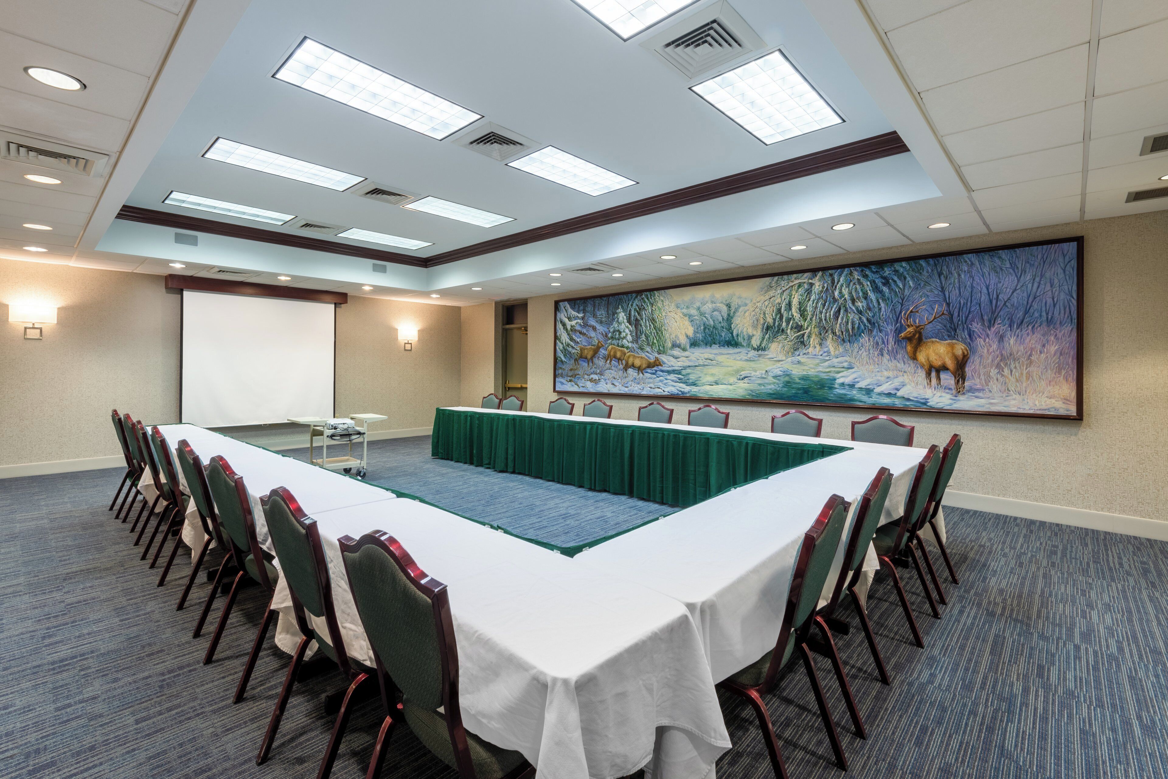 A conference room with a long table, chairs, a projector screen, and a large mural of a winter scene.
