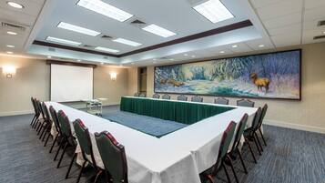 A conference room with a long table, chairs, a projector screen, and a large mural of a winter scene.