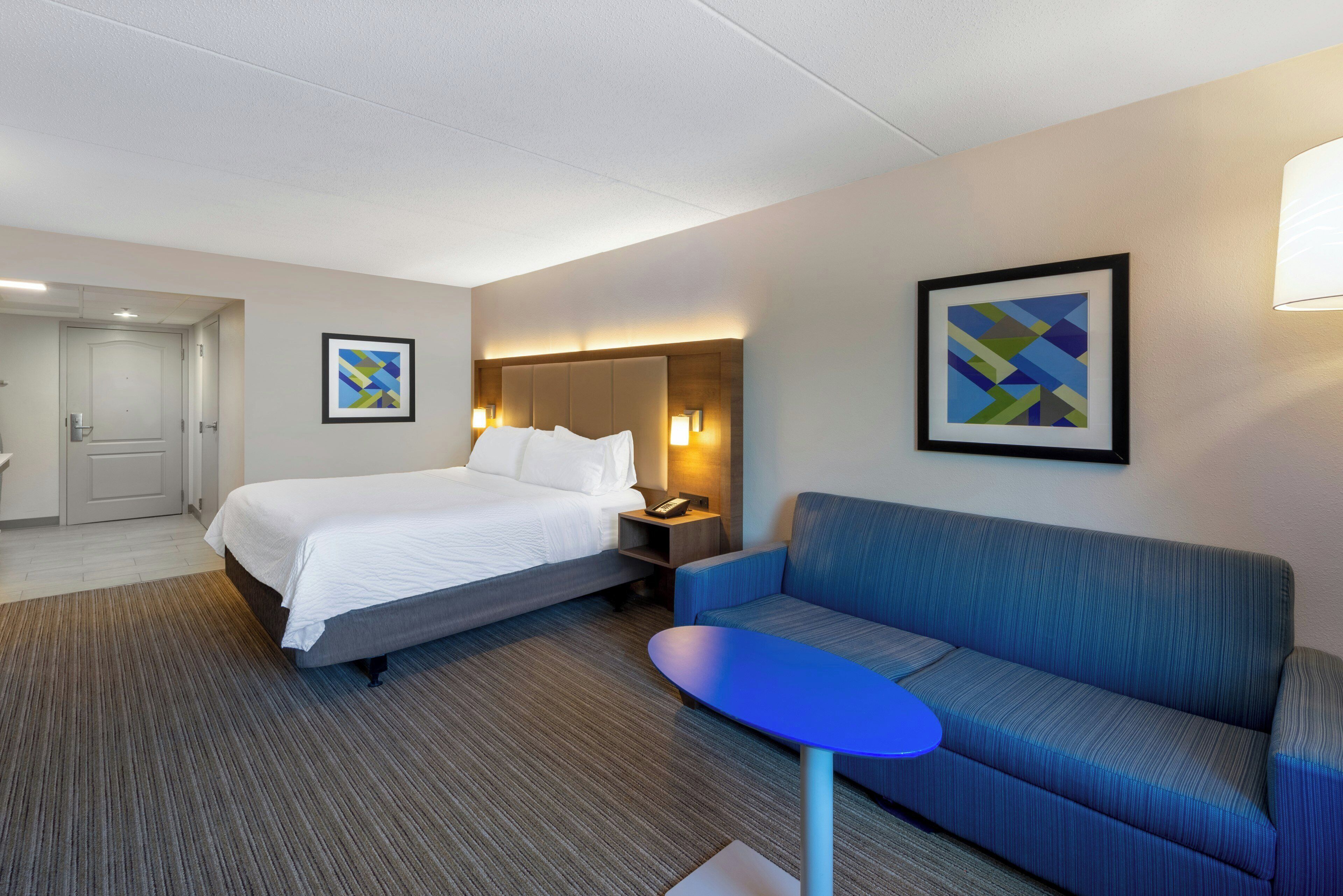 A hotel room with a bed, a sofa, a small table, and two wall-mounted lamps.