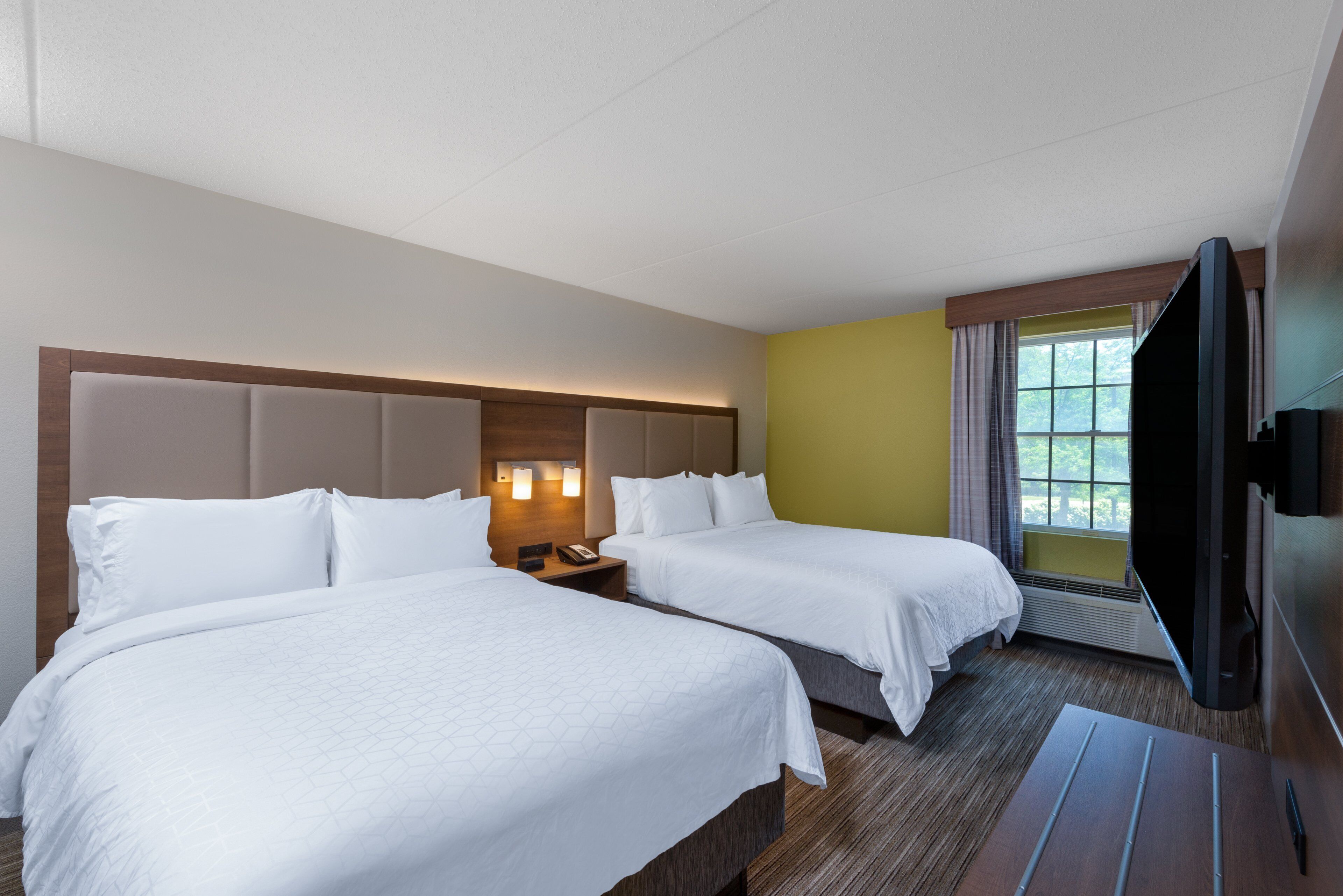 Habitación de hotel con dos camas, un televisor de pantalla plana, una ventana con cortinas y un teléfono instalado en la pared.