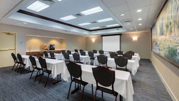 A conference room with multiple tables and chairs, a projector screen, and a painting on the wall.