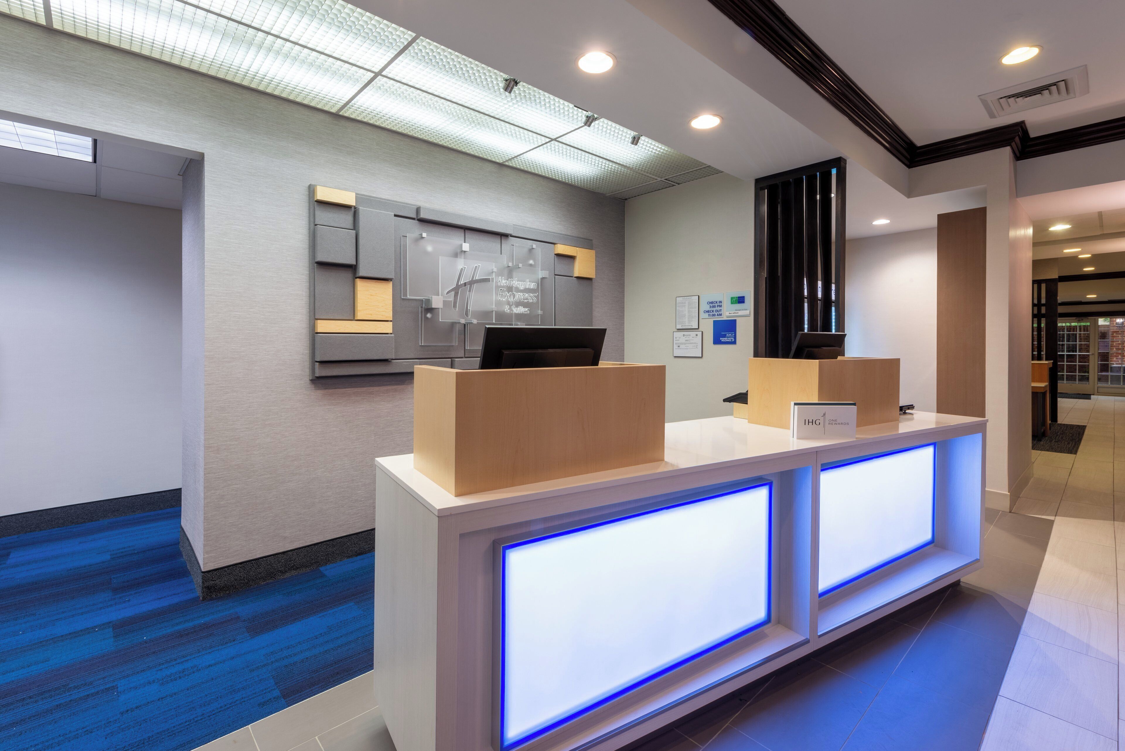 A hotel reception desk with a modern design, featuring a check-in counter, a digital display, and a sign indicating the hotel name.