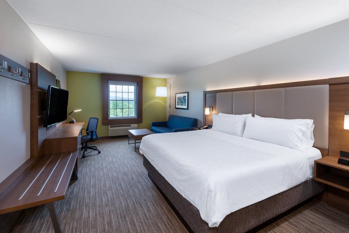A hotel room with a large bed, a desk with a chair, a TV, a window with a view, and a blue sofa.