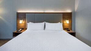 A hotel room with a large bed, two bedside tables, and wall-mounted lamps.