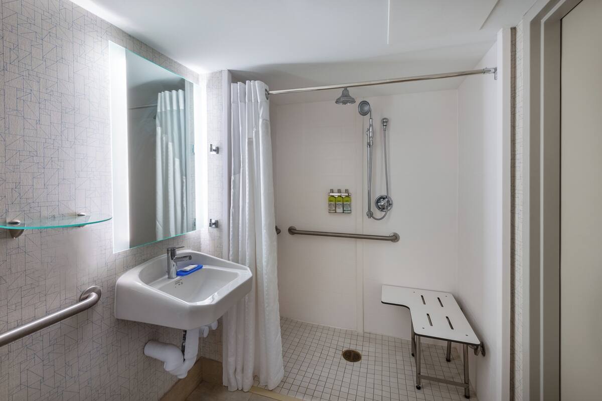 A modern bathroom with a glass shower enclosure, a white sink with a blue soap dispenser, and a grab bar.