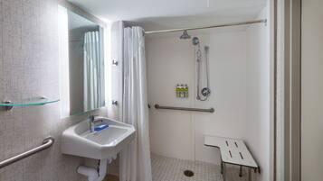 A modern bathroom with a glass shower enclosure, a white sink with a blue soap dispenser, and a grab bar.