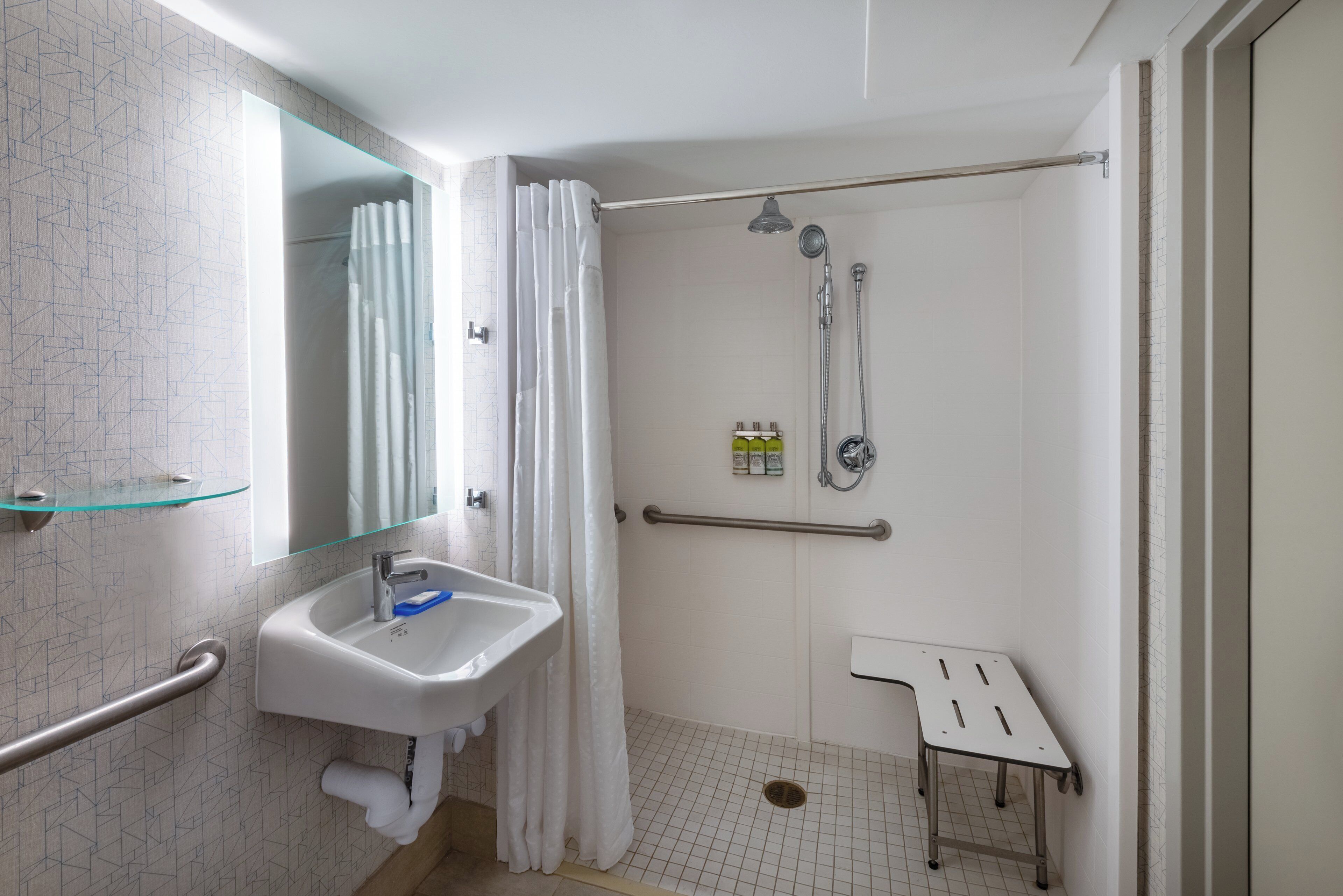 A bathroom with a glass shower enclosure, a white sink, a mirror, and a grab bar.