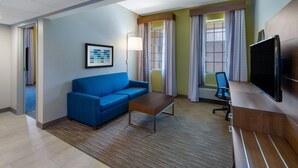 A hotel room with a blue sofa, a wooden coffee table, a TV, and a desk with a chair.