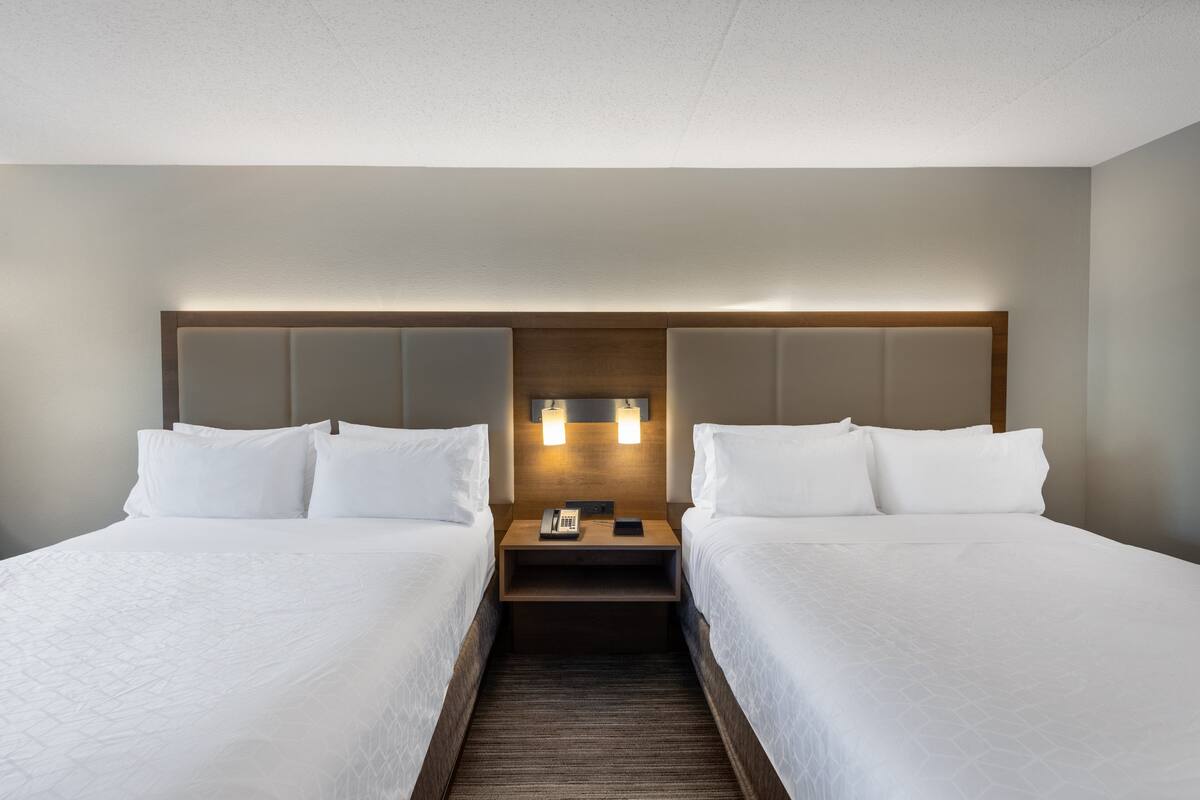 A hotel room with two single beds, a wooden headboard, bedside tables with lamps, and a neutral color scheme.