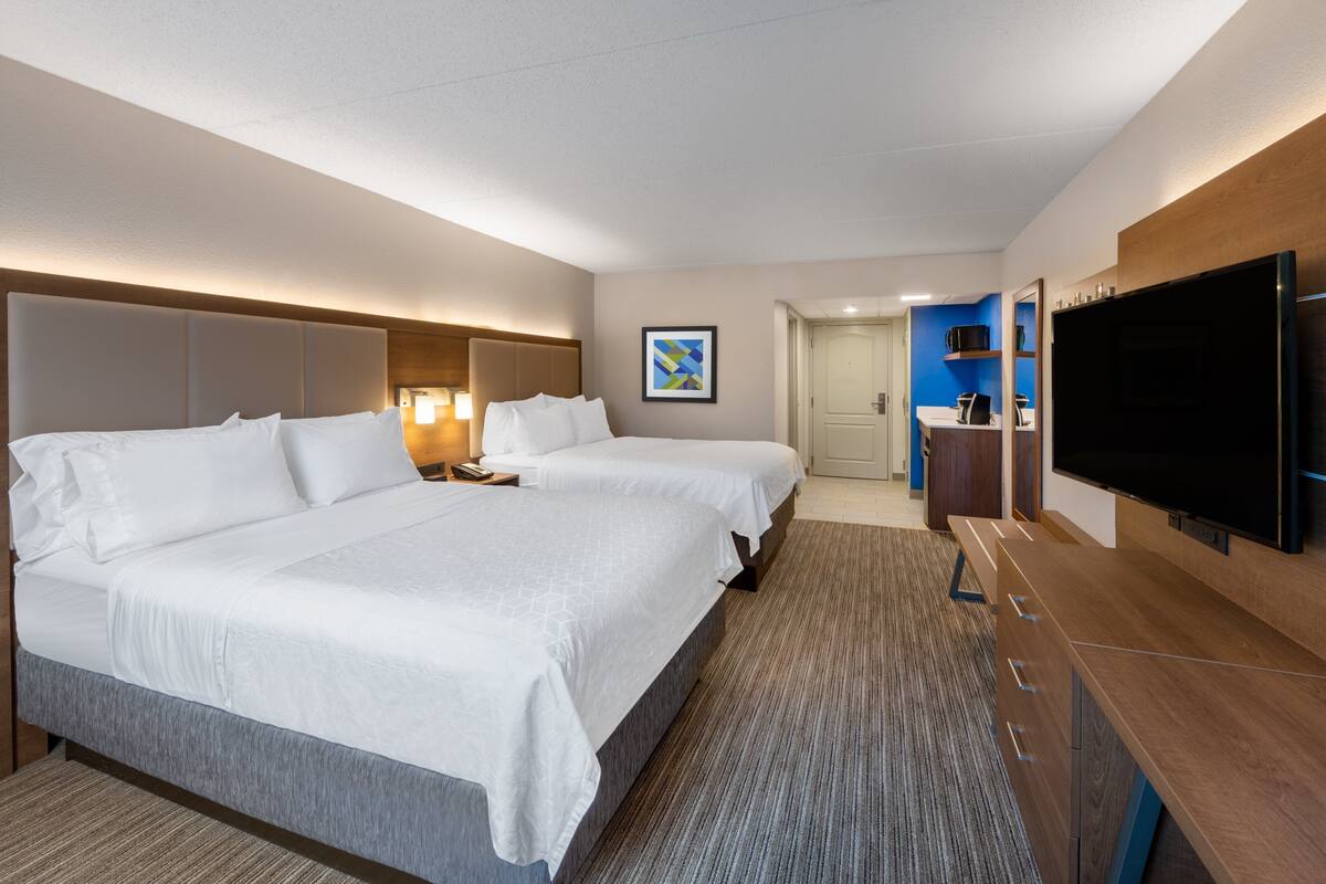 A hotel room with two beds, a flat-screen TV, a desk, and a bathroom visible through an open door.