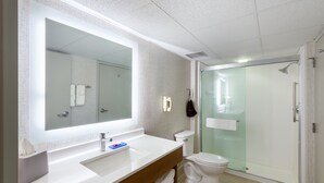 A modern bathroom with a large mirror, white sink, and glass-enclosed shower.