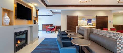 A hotel lobby with a fireplace, television, seating area, and a bar.
