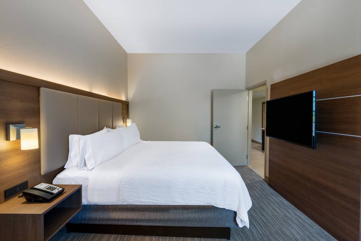 A modern hotel room with a large bed, a flat-screen TV mounted on the wall, and a bedside table with a phone.