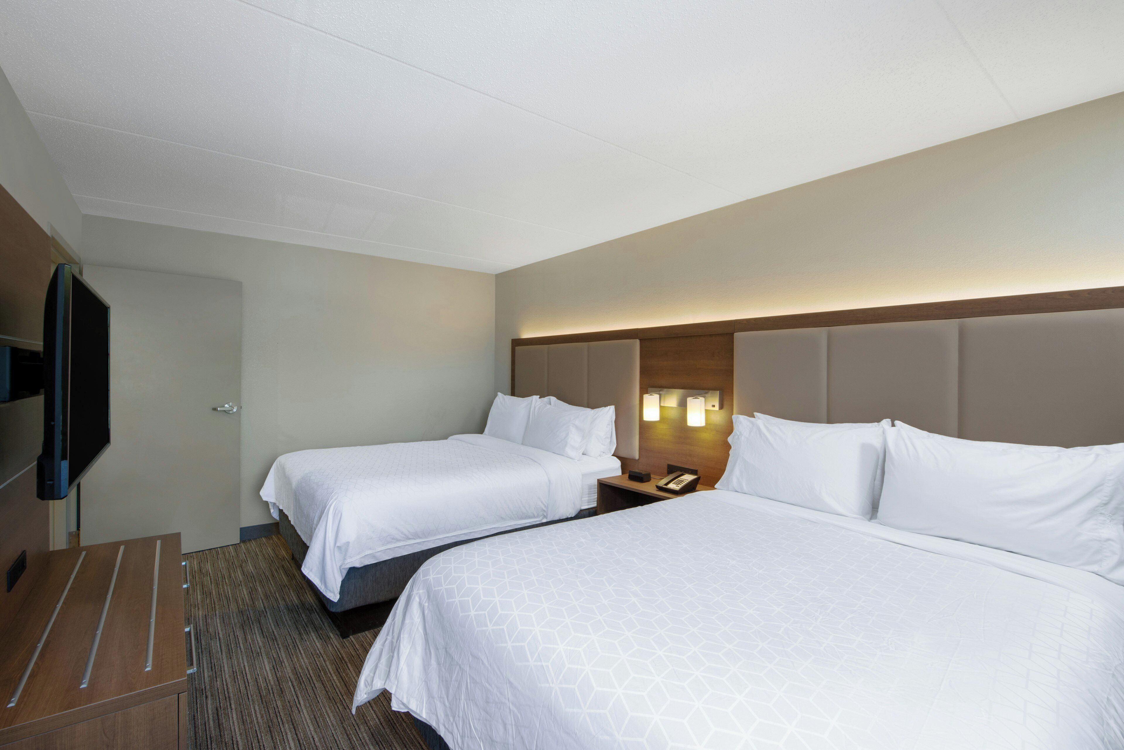 A hotel room with two beds, a flat-screen TV, and a wooden desk.