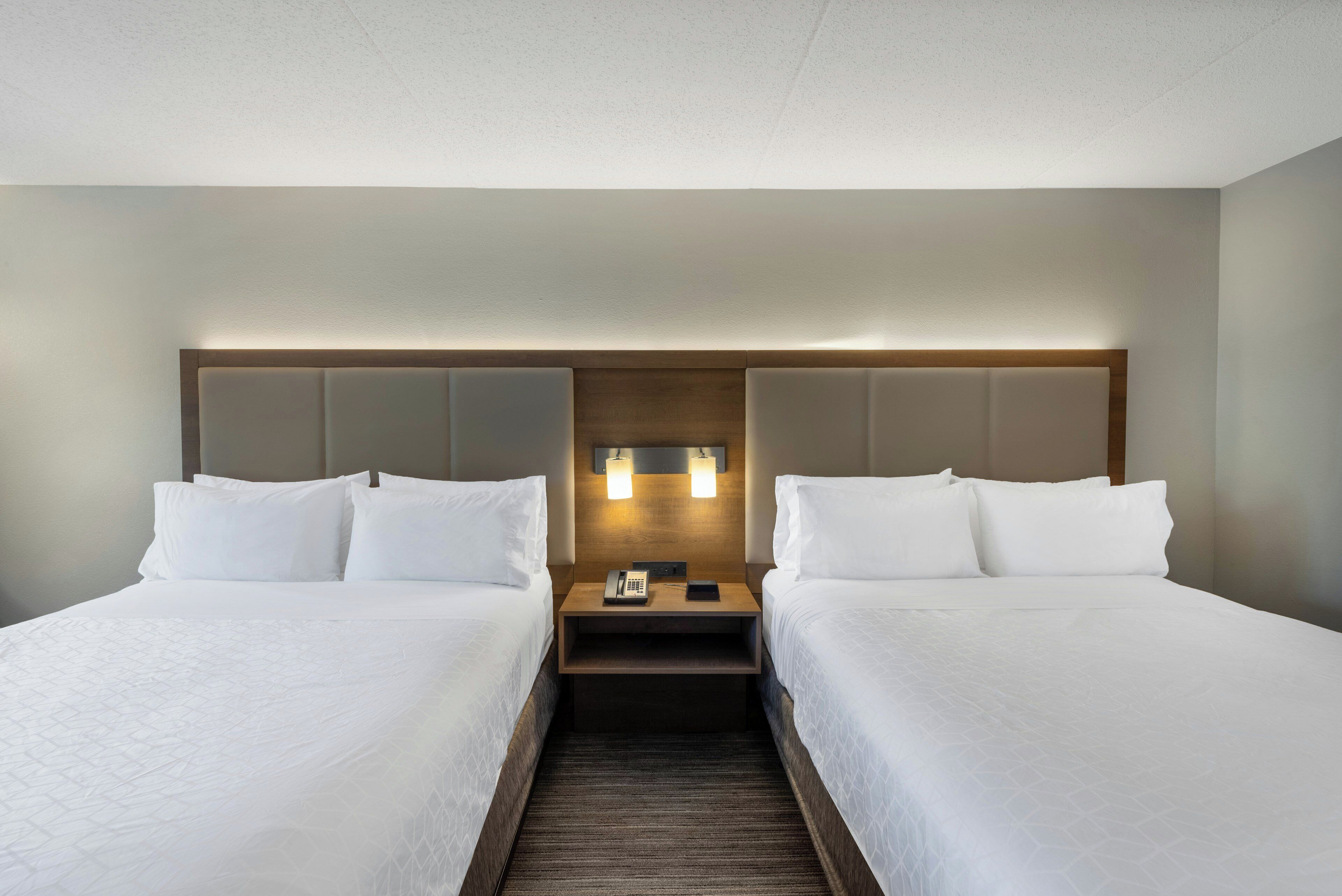 Een hotelkamer met twee bedden, een houten hoofdeinde, een nachtkastje met telefoon en een wandlamp.